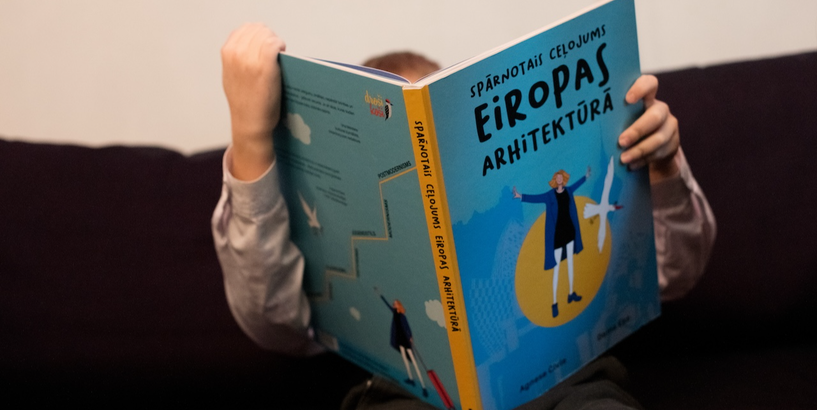 Grāmatas “Spārnotais ceļojums Eiropas arhitektūrā” atvēršanas svētkos mazs zēns iegrimis grāmatas pētīšanā