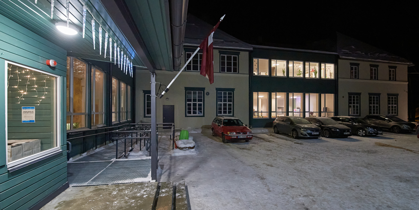 Jaunciema pamatskolas ārskats ar Latvijas karogu pie ieejas durvīm un automašīnām pagalmā