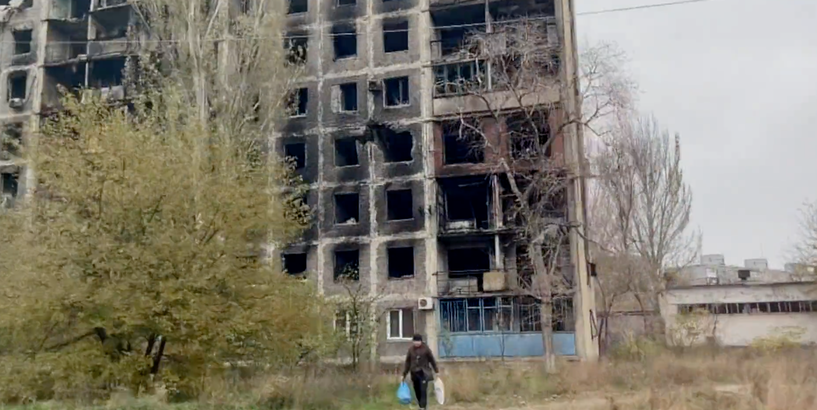 Fonā kara darbības rezultātā sagrauta ēka ar sievieti, kura nes iepirkuma tīkliņus