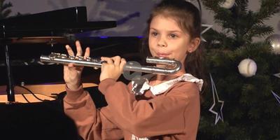 Ziemassvētku eglītes fonā mūzikas skolas audzēkne spēlē flautu